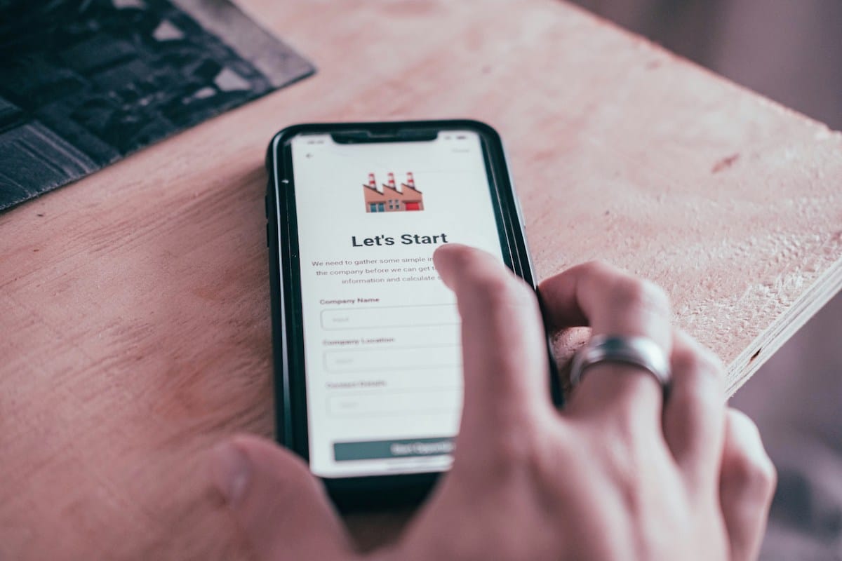A person holds a smartphone displaying an online form titled "Let's Start" with fields for company name and location.