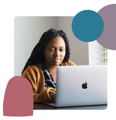 A person with long plaited hair sits at a table, looking at an open Apple laptop. Abstract coloured shapes are overlaid in the corners of the image. Light streams in from a window on the right.