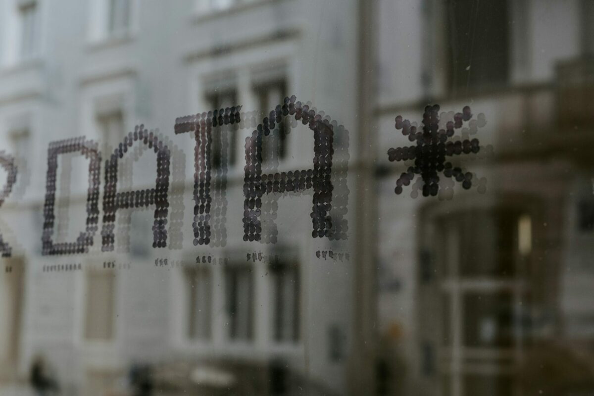 The word "DATA" with an asterisk is written in a pixelated style on a window. A blurred building facade is visible through the glass. Industrial feel.