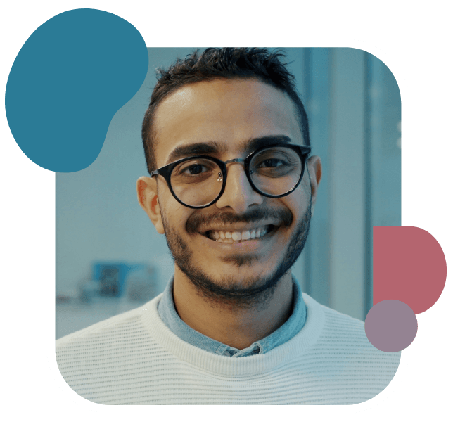 Young man with glasses and a friendly smile, wearing a white sweater. Background is softly blurred, featuring blue and pink abstract shapes.