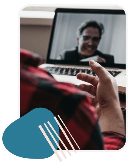 A person in a red plaid shirt gestures towards a laptop showing a man smiling during a video call, conveying a tone of connection and engagement.